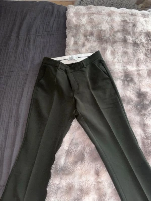 Kostymbyxor från Neo Noir - Säljer ett par mörkgröna kostymbyxor från Neo Noir i modellen Cassie Pants. Byxorna har pressveck, bälteshällor och är tillverkade i mjuk polyesterblandning med lite stretch för skön passform.