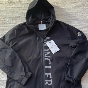 Moncler windbreaker - Säljer en stilren svart windbreaker från Moncler. Perfekt inför våren. Storlek M i nyskick med tag. Köpt från en vän kan inte garantera äkthet därför priset.