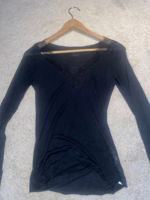 Svart långärmad topp från Intimissimi - Säljer en svart långärmad topp från Intimissimi med vacker spetsdetalj vid v-ringningen och axlarna. Toppen är i mjukt material med inslag av kashmir, vilket gör den extra skön att bära. Perfekt för dig som gillar stilrena plagg med en twist.