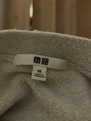 Beige kofta från Uniqlo med knappar - Mysig beige kofta från Uniqlo i storlek XS. Koftan är croppad med stora bruna knappar framtill och har en avslappnad passform. Tillverkad i ett mjukt stickat material och har långa ärmar med ribbade muddar. Perfekt för lager på lager under hösten.