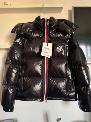 Moncler Montbéliard Dunjacka – Svart – Ny med taggar - Moncler Montbéliard Giubbotto i svart, storlek 3 (M/L). Helt ny med taggar, aldrig använd.  ✔ QR/NFC-chip ✔ Originaltaggar & inneretiketter ✔ Kvitto finns ✔ 100 % äkta  Populär Moncler-modell i blank nylon med varm dunfyllning. Perfekt vinterjacka som håller värdet bra.  📦 Skickas spårbart eller möts upp 💬 Skriv vid seriöst intresse 