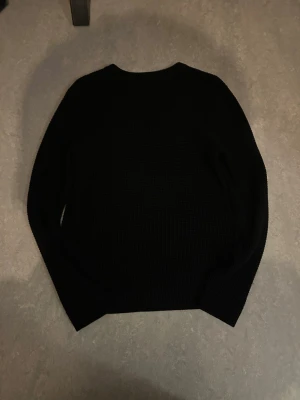 Svart stickad tröja från H&M - En svart stickad tröja från H&M med rund halsringning och långärmad passform. Tröjan har en grovstickad struktur som ger en schysst textur och är perfekt för kyligare dagar. Enkel och stilren design som funkar till det mesta.