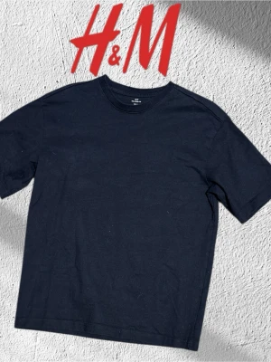 Svart basic t-shirt från H&M - En enkel svart t-shirt från H&M med klassisk rund hals och normal passform. Tillverkad i mjuk bomull som känns skön mot huden. Perfekt till jeans eller shorts för en clean och stilren look. Storlek S