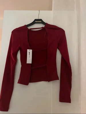 Vinröd topp med öppen rygg - Helt ny vinröd långärmad topp från Gina Tricot med öppen rygg och detaljer.  Toppen har en figurnära passform och är tillverkad i ett mjukt stretchigt material. Storlek 34 och prislapp kvar!