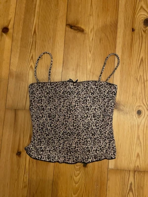Leopardmönstrad linnetopp från Bershka - Säljer en snygg leopardmönstrad linnetopp från Bershka i storlek XS. Toppen har tunna axelband, liten rosett framtill och är i ett stretchigt, mjukt material. Perfekt att styla med jeans eller kjol för en trendig look.