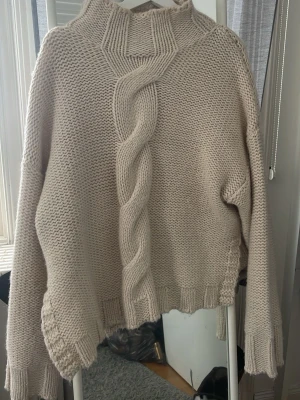 Beige stickad tröja från Zara - Säljer en chunky beige stickad tröja från Zara med grov fläta framtill och hög krage. Tröjan har långa ärmar, ribbade muddar och en loose fit som ger en avslappnad vibe. Perfekt för kyliga dagar och enkel att styla med jeans eller kjol.