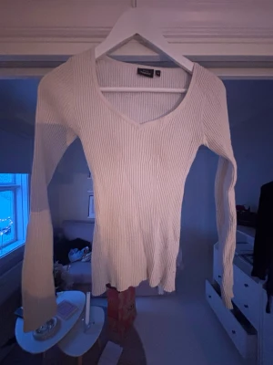 Ribbad beige långärmad topp  - Säljer en beige ribbad topp med lång ärm och snygg v-ringad hals. Materialet är mjukt och stretchigt, perfekt för att styla med jeans eller kjol. Enkel och stilren design som funkar till många looks.