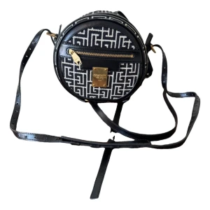 Balmain väska äkta  - Snygg rund ryggsäck från Balmain i svart och vitt med grafiskt mönster. Väskan har justerbara axelremmar, guldfärgade metalldetaljer och dragkedja framtill. Materialmix av skinn och textil ger en lyxig känsla och modern look. Finns äkthetsbevis.