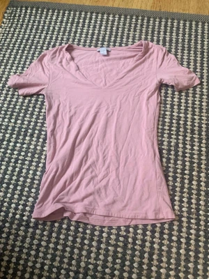 Ljusrosa v-ringad t-shirt - Enkel och mjuk ljusrosa t-shirt med v-ringning och korta ärmar. T-shirten har en slim passform och är tillverkad i bomull, perfekt för en avslappnad och stilren look.