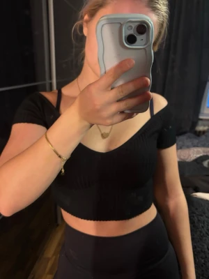 Svart croppad ribbad topp  - Säljer en svart ribbad croppad topp från Zara med v-ringning och offshoulder-design. Toppen är i mjuk bomullsmix och har korta ärmar. Storlek S men passar även XS. Nästintill oanvänd