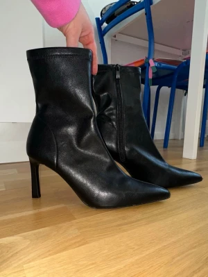 Svarta stövletter från Stradivarius - Säljer ett par svarta stövletter från Stradivarius. De har spetsig tå, smal hög klack och dragkedja på sidan. Snygg minimalistisk design som passar till många outfits. Perfekta för dig som gillar stilrena boots med lite edge. Aldrig använda.