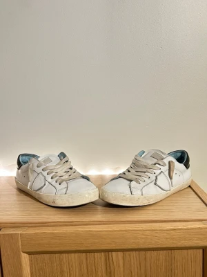  Philippe Model junior box ingår storlek 38 - Säljer ett par vita Philippe Model sneakers i skinn med grå snörning och svart detalj på hälen. Skorna har en klassisk låg profil, rund tå och platt sula. Perfekta för dig som gillar stilrena och tidlösa sneakers med en touch av street.