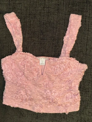 Rosa spetsig linnetopp i storlek small - Supersöt rosa linnetopp från Amisu med breda axelband och blommig spets över hela toppen. Croppad modell med lätt v-ringad detalj framtill. Storlek small, mycket fint skick då den knappt är använd 