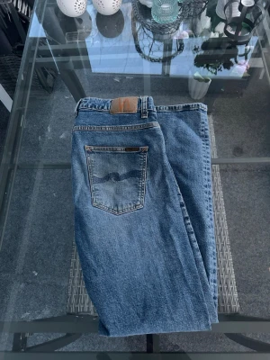 Nudie Jeans Grim Tim – Broken FadedW33 L32 - Snygga Nudie Jeans Grim Tim i tvätten Broken Faded. Klassiska blå jeans med rak/slim passform och lätt stretch som sitter riktigt bra. Clean vintage-look som passar perfekt till streetwear och vardagsfits.  • Modell: Grim Tim • Storlek: W33 L32 • Passform: straight / slim • Färg: blå faded denim • Material: 99% bomull, 1% elastan • Skick: bra begagnat skick, naturlig fade  Perfekta året runt 🔥 