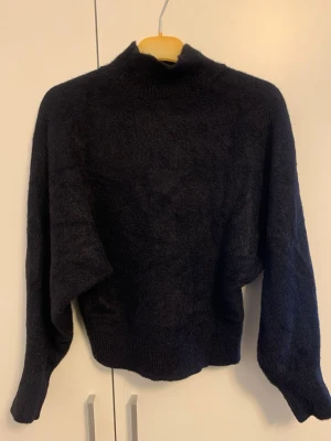 Svart stickad polotröja - Mysig svart stickad polotröja med lång ärm och lite loose passform. Perfekt för kyliga dagar och enkel att matcha med jeans eller kjol. Hög hals ger extra värme och stil.