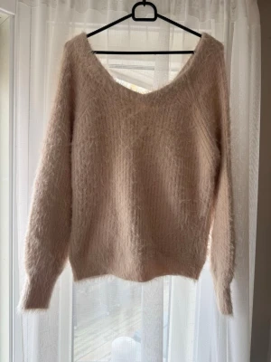 Hårig stickad tröja från Bik bok balance  - Supermjuk och fluffig stickad tröja i ljusbeige/rosa ton. Tröjan har en bred v-ringad hals och långa ärmar. Den har en loose passform och är perfekt för mysiga dagar. Hårig stickad tröja. Materialet är stickat och ger en skön och varm känsla. Sparsamt använd. 
