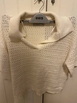 Vit stickad polotopp - Säljer en vit stickad polotopp i storlek XS. Toppen har korta ärmar, krage och ett hålmönster över hela plagget som ger en luftig känsla. Perfekt till sommaren och enkel att styla med både jeans och kjol.