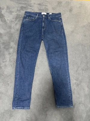 Blå jeans från Calvin Klein - Säljer ett par klassiska blå jeans från Calvin Klein Jeans. Modellen har raka ben, fem fickor och normal midja. Jeansen är i ett mjukt bomullsmaterial och har diskreta sömmar samt logga på bakfickan. Perfekta till en avslappnad stil.