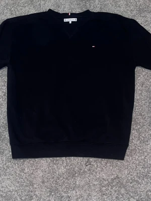 Svart sweatshirt från Tommy Hilfiger - Säljer nu en lite schysstare Tommy Hilfiger tröja. Storleken är 164 men passsar absolut om mot 175 då den är en lite större modell. Ber om ursäkt för dåliga bilder, hade ej möjlighet till bättre ljus tyvärr… Tröjan är i fint skick och funkar lika på ute som att vara hemma och chilla.  Perfekt för dig som gillar klassisk och enkel stil.