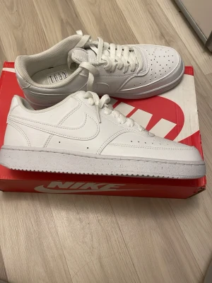Vita Nike Air Force 1 sneakers - Säljer ett par klassiska vita Nike Air Force 1 sneakers med lågt skaft. Skorna har snygg snörning, perforerad tå och är tillverkade i skinn. Perfekta för dig som vill ha en clean och tidlös look. Kommer i originalkartong.