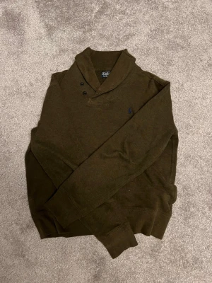 Olivgrön tröja från Polo Ralph Lauren - Säljer en olivgrön långärmad tröja från Polo Ralph Lauren med klassisk broderad logga på bröstet. Tröjan har en snygg krage med knappar och är gjord i mjukt bomullsmaterial. Perfekt till jeans för en clean och stilren look.