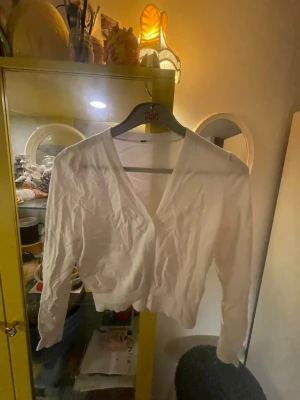 Vit omlottkofta i bomull, stl S - Säljer en vit omlottkofta i mjuk bomull. Koftan har v-ringad hals, långa ärmar och croppad passform. Perfekt att slänga över ett linne eller topp. Enkel och passar till det mesta.
