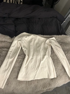 Vit långärmad offshoulder topp i bomull - En enkel och stilren vit långärmad offshoulder topp med rund hals. Modellen är figurnära och passar perfekt till jeans eller kjol. Tillverkad i mjuk bomull som känns skön mot huden. Perfekt basplagg för alla tillfällen.