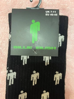 Billie Eilish Sockor – Oöppnade | Svart med Blohsh-logo | EU 40-45 / UK 7-11 - Helt nya, officiella Billie Eilish-sockor. Svarta med vita Blohsh-loggor. Oanvända och fortfarande i originalförpackning. Perfekta för fans eller som present.  Storlek: EU 40-45 / UK 7-11 Skick: Nytt / Oöppnat paket