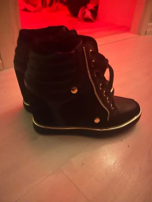 Svarta sneakers med gulddetaljer - Säljer ett par svarta wedge sneakers från Anna field, skit snygga med guld detaljer och en högre klack lite Isabel marant likande, de är i storlek 37 men passar nog bättre som storlek 38. Knappt använda.