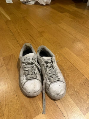 Vita sneakers från Polo Ralph Lauren - Klassiska vita sneakers från Polo Ralph Lauren med logga på sidan och mörkblå detalj vid hälen. Skorna har snörning med vita skosnören där det står 'Polo' tryckt i mörkblå. Tillverkade i skinn med platt sula och rund tå.