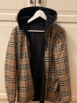 Burberry windbreaker - Snygg vindjacka från Burberry med klassiskt beige rutmönster och svart insida. Jackan är vändbar med dragkedja, två fickor och huva. Storlek S. Bra skick. Pris kan diskuteras vid snabb affär!