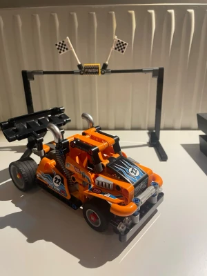 LEGO Technic Racingbil 42104 - Säljer en LEGO Technic racingbil, modell 42104. Bilen är orange med svarta och blå detaljer, har stora bakhjul, sportig bakvinge och coola dekaler med nummer 22. Byggsatsen innehåller även ett målgångsmål med rutiga flaggor. Perfekt för dig som gillar fartfyllda byggen!
