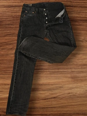 Levi's 501 jeans med knappar - Klassiska svarta Levi's 501 jeans med rak passform och knappgylf. Jeansen har fem fickor och är tillverkade i kraftig denim. Perfekta för en avslappnad och tidlös look.