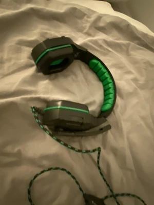 Svarta och gröna gaminghörlurar - Säljer svart gröna gaming hörlurar minns inte märket är jätte bra men vänstra sidan låtet inte så mycket men de funkar som de ska!