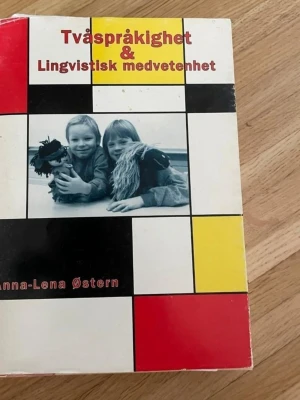 Tvåspråkighet & Lingvistisk medvetenhet - Bok med titeln 'Tvåspråkighet & Lingvistisk medvetenhet' av Anna-Lena Østern. Omslaget har ett färgglatt rutmönster i rött, gult, svart och vitt samt ett svartvitt foto på två barn med handdockor. Boken är tryckt på matt papper och har mjuka pärmar. Mest omslaget som är lite slitet.