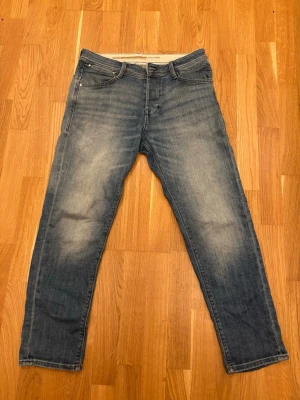Unik blåfärgade jeans från Jack & Jones aldrig använda!  - Säljer ett par unikt blåa jeans från Jack & Jons med snyggt färgade  detaljer och raka ben. Jeansen har fyra fickor, ljus tvätt och kontrastsömmar på bakfickorna. Perfekta för en avslappnad och lugn fit. Tapered fit. 