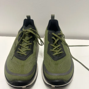 Olivgröna sneakers från Ecco 41 - Snygga olivgröna sneakers från Ecco med svarta och grå detaljer. Ovandelen är i textil med förstärkningar i syntet och reflekterande detaljer. Skorna har vita sulor och klassisk snörning. Perfekta för en sportig och trendig look.
