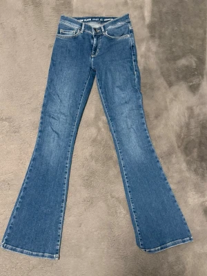 Blå low flare jeans XS längd 31 - Snygga blå jeans med low flare-modell och klassisk femficksdesign. Midjan är låg och benen har en utsvängd passform. Storlek XS och längd 31. 