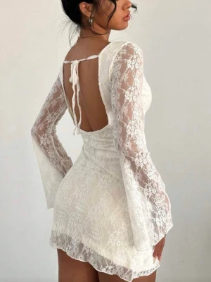 Student klänning  - Kort vit klänning i spets med långa, utsvängda ärmar och öppen rygg som knyts med band. Klänningen har figurnära passform och romantisk känsla tack vare spetsmaterialet. Perfekt för dig som gillar en feminin och trendig stil.