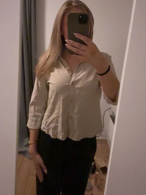 Beige skjorta med trekvartsärm - Stilren beige skjorta med trekvartsärm och klassisk krage. Skjortan har knappar framtill och en avslappnad passform, perfekt för en enkel och clean look.