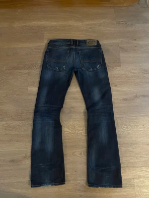 Mörkblå diesel jeans bootcut - Snygga mörkblå jeans från diesel med bootcut-passform. Jeansen har klassisk femficksdesign, slitningar och ljusare partier framtill och baktill för en cool, använd look. Perfekta för dig som gillar en avslappnad men trendig stil.