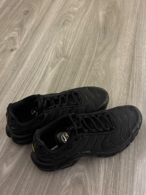 Svarta Nike Air Max Plus sneakers - Säljer ett par helsvarta Nike Air Max Plus sneakers med klassisk vågig design och synlig Air-dämpning i sulan. Skorna har använts 2-3 gånger sen ba legat i förrådet då dom vart för stora och inte passat. Dessa skor är inte mina utan mitt syskon  som är tonåring så de må se lite slitet ut där framme men de händer när man är ute och går men de verkligen bra skick köptes för 2000kr  