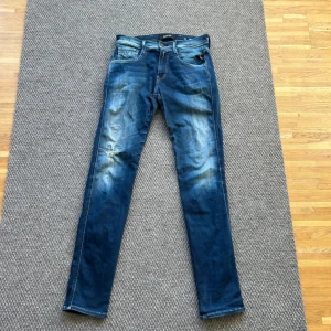 Replay Anbass jeans  - Säljer ett par Replay Anbass jeans i blå tvätt med snygga slitningar. Klassisk femficksmodell med dragkedja och knapp, samt Replay-logga på linningen.