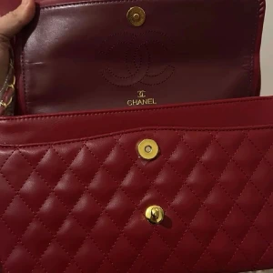 Röd Classic Flap handväska - Säljer en ikonisk röd Classic Flap handväska i quiltat läder med guldfärgade metalldetaljer och kedjerem. Väskan har det klassiska CC-spännet framtill och dubbla innerfack. Perfekt för dig som vill ha en tidlös och lyxig accessoar.