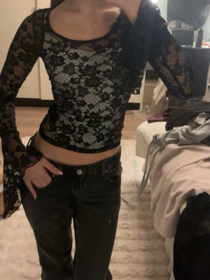 Svart spets topp - Säljer en snygg svart topp i spets med blommigt mönster. Toppen är genomskinlig, har långa vida ärmar och en tight passform. (Har linne under)