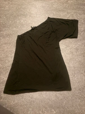 Svart asymmetrisk topp - Säljer en svart topp med asymmetrisk design och en ärm. Toppen har en trendig off-shoulder-look och är gjord i ett mjukt, stretchigt material som sitter snyggt på kroppen. Perfekt för dig som vill ha något lite extra till din outfit.