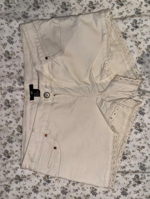 Beiga shorts med spetsdetaljer H&M - Snygga beiga shorts från H&M med spetsdetaljer längs bensluten. Shortsen har en relativt låg midja.
