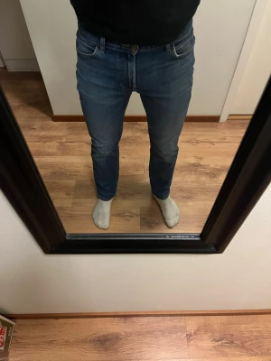 Blå Lee slim fit jeans - Säljer ett par klassiska blå slim fit jeans med fem fickor och normal midja. Jeansen har en snygg tvätt och raka ben, perfekta till en avslappnad stil. Materialet är denim och de har en enkel design utan slitningar.