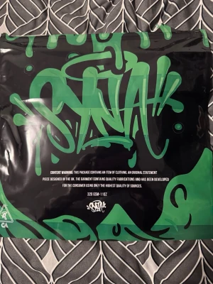 Svart mössa från Synawear - Snygg svart mössa från Synawear med broderad logga framtill. Tillverkad i mjukt tyg som sitter skönt på huvudet. Perfekt för dig som gillar streetwear och vill ha en stilren accessoar med unik touch.