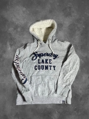 Grå Superdry hoodie med teddyfoder - Tvär snygg superdry hoddie med fodrad luva perfekt tills när det blir för varmt med jacka. Såklart villig att förhandla vid snabb affär! Skriv med minsta lilla fråga!  